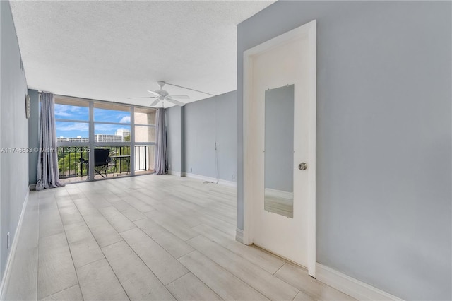 spare room featuring expansive windows, a textured ceiling, a ceiling fan, and baseboards