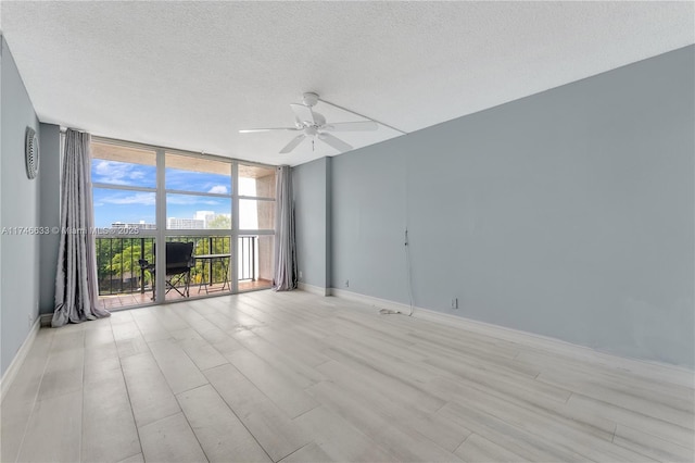 empty room with light wood-type flooring, baseboards, floor to ceiling windows, and a textured ceiling