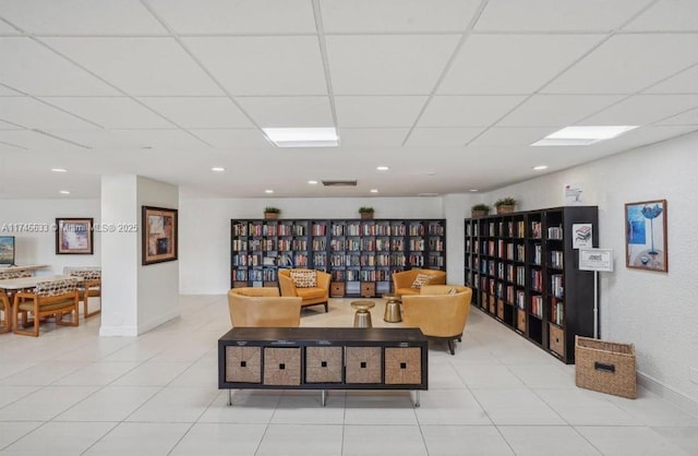 living area featuring wall of books, light tile patterned floors, baseboards, and a drop ceiling