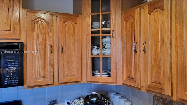 room details featuring glass insert cabinets, black microwave, and backsplash