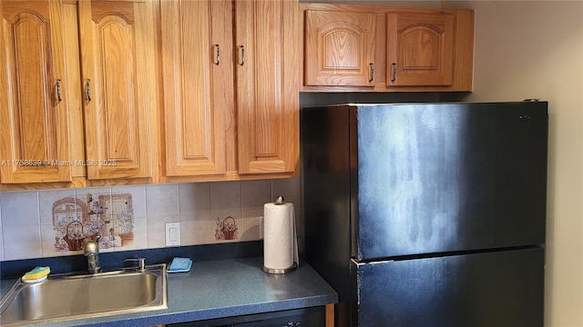 kitchen with dark countertops, tasteful backsplash, a sink, and freestanding refrigerator