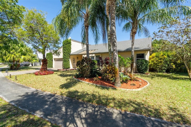 view of front of house with stucco siding, a front lawn, a garage, and driveway