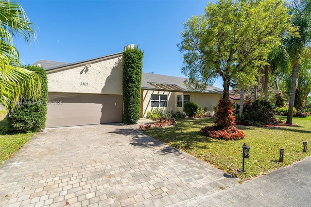 ranch-style house featuring a pergola, stucco siding, a front lawn, a garage, and decorative driveway