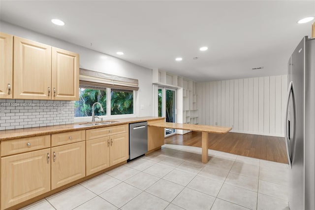 kitchen with light brown cabinets, light tile patterned floors, decorative backsplash, appliances with stainless steel finishes, and a sink