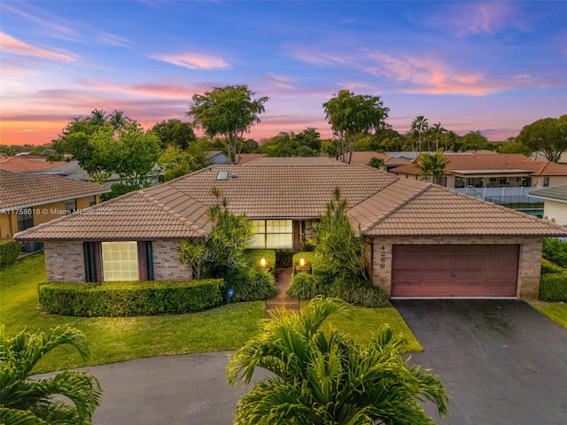 view of front of house featuring a garage, a tiled roof, brick siding, and a front yard