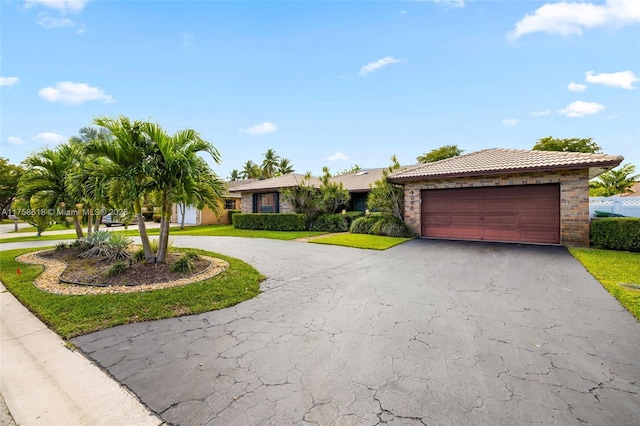 ranch-style home featuring an attached garage, aphalt driveway, a front yard, and a tile roof