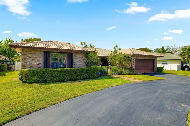 single story home featuring a front lawn, a tile roof, an attached garage, and aphalt driveway