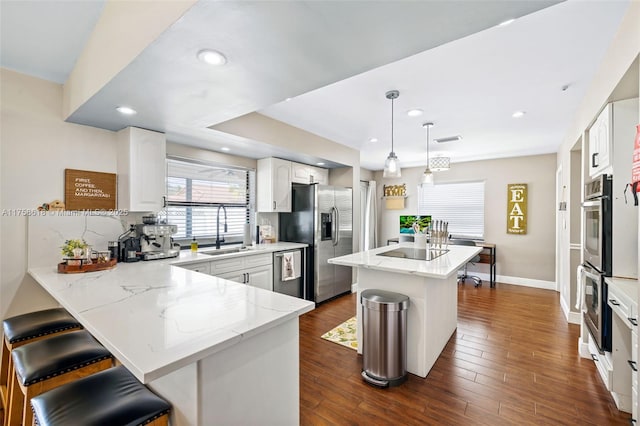 kitchen with a peninsula, a sink, appliances with stainless steel finishes, light stone countertops, and dark wood-style floors