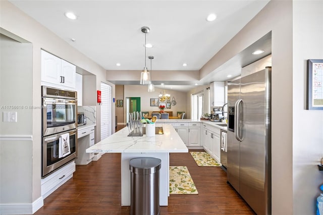 kitchen with a center island, dark wood finished floors, hanging light fixtures, appliances with stainless steel finishes, and white cabinets