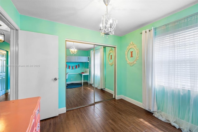 unfurnished bedroom with a notable chandelier, a closet, baseboards, and wood finished floors