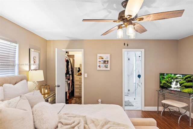 bedroom featuring a walk in closet, a ceiling fan, ensuite bath, wood finished floors, and baseboards