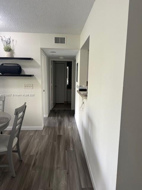 hall featuring dark wood-type flooring, visible vents, a textured ceiling, and baseboards