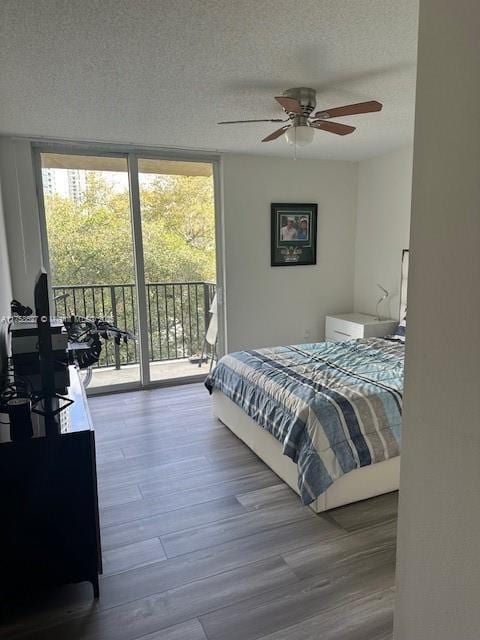 bedroom featuring ceiling fan, a textured ceiling, wood finished floors, access to exterior, and expansive windows