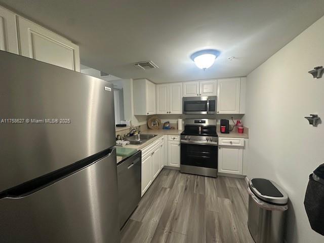 kitchen featuring stainless steel appliances, a sink, visible vents, white cabinetry, and light countertops