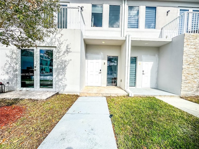 entrance to property with french doors, a lawn, a balcony, and stucco siding