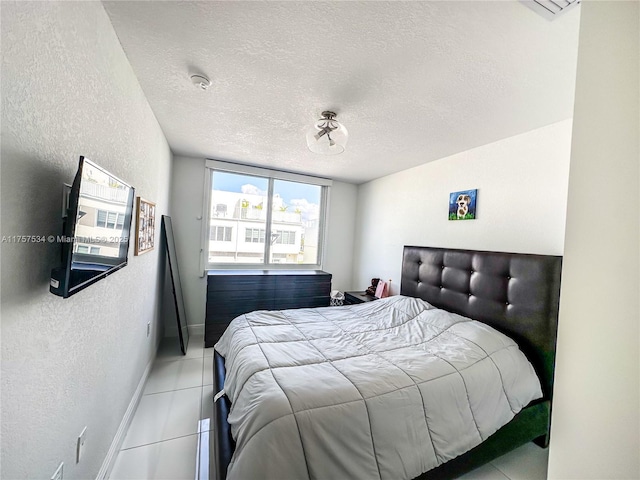 bedroom featuring light tile patterned flooring, a textured wall, a textured ceiling, and baseboards