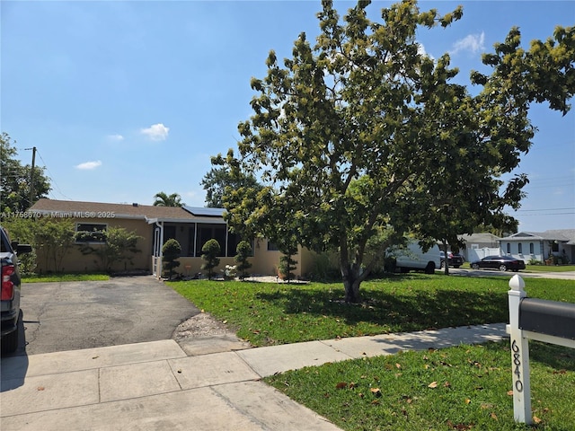 view of front facade with aphalt driveway, solar panels, a front yard, and stucco siding