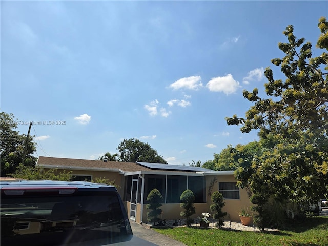 view of front of property featuring solar panels, a sunroom, and stucco siding