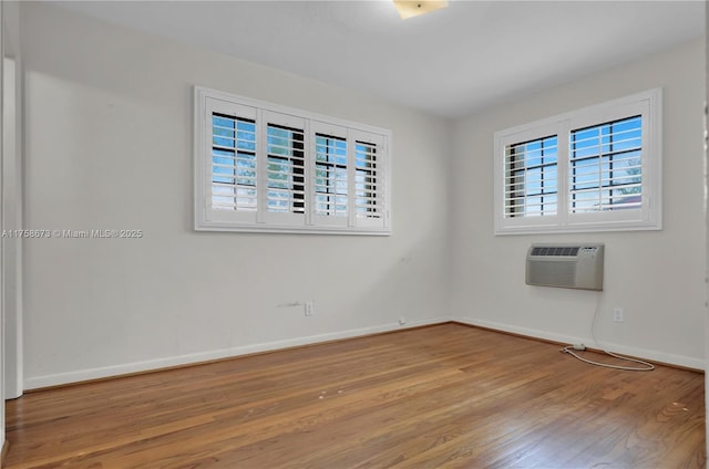 spare room with a wall unit AC, baseboards, and wood finished floors