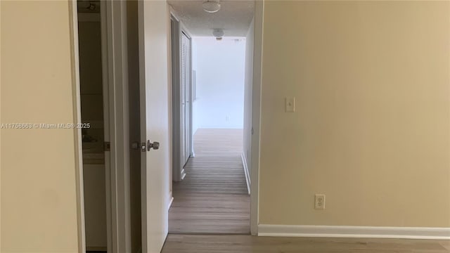 hall with a textured ceiling, wood finished floors, and baseboards