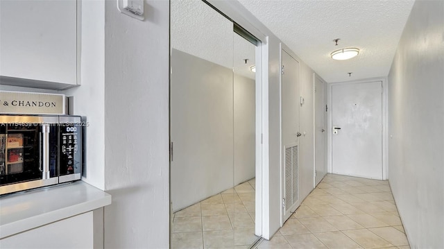 hall with visible vents, light tile patterned flooring, and a textured ceiling