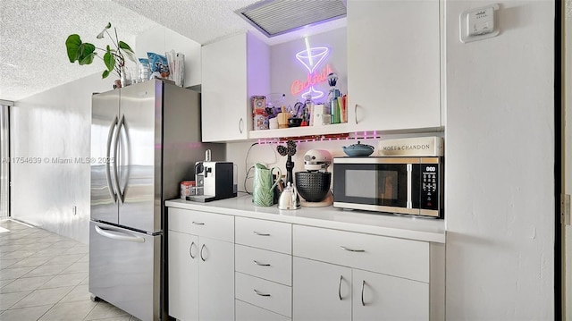 kitchen with light tile patterned floors, white cabinetry, appliances with stainless steel finishes, and a textured ceiling