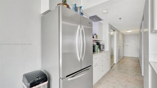 kitchen with a textured ceiling, light tile patterned floors, white cabinets, light countertops, and freestanding refrigerator