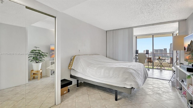 bedroom featuring a wall of windows, access to outside, a textured ceiling, and light tile patterned floors