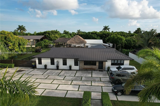 back of house featuring metal roof, fence, stone siding, stucco siding, and a standing seam roof