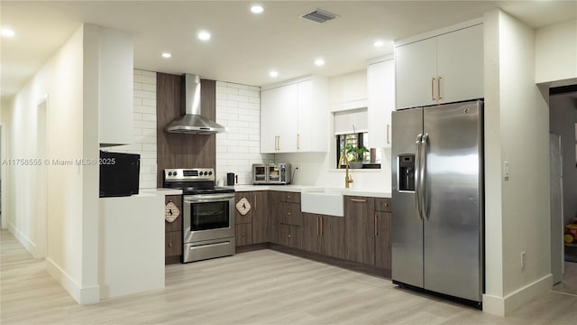 kitchen featuring light countertops, appliances with stainless steel finishes, light wood-type flooring, decorative backsplash, and wall chimney exhaust hood