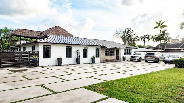 view of front facade with metal roof, fence, stucco siding, a front lawn, and a standing seam roof