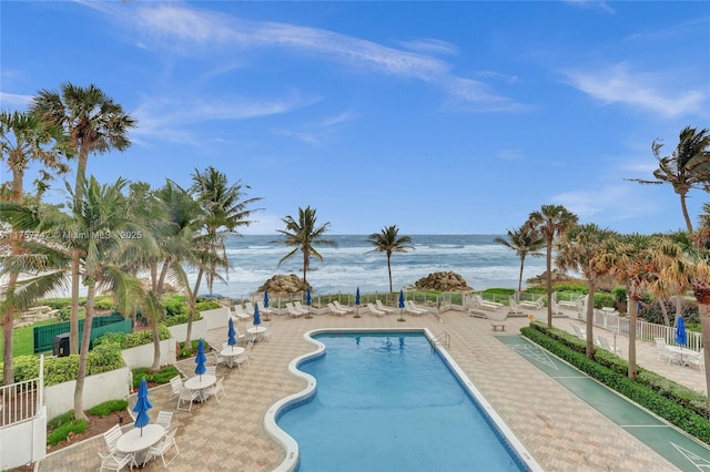 pool featuring a patio, a water view, and fence