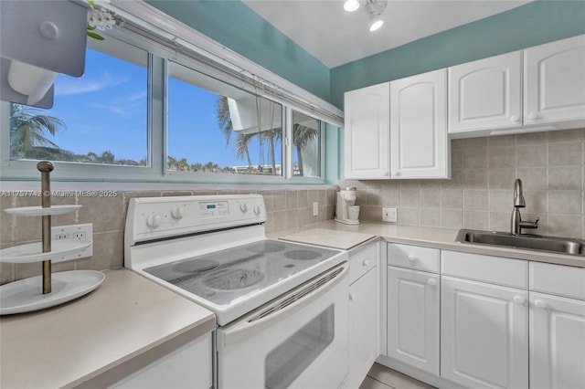 kitchen with backsplash, electric range, white cabinets, and a sink