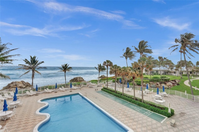 community pool featuring a water view, a patio area, and fence