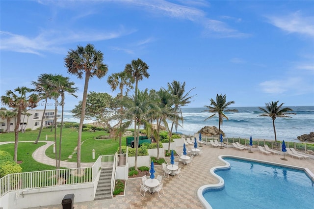 community pool featuring a beach view, a lawn, a patio, a water view, and fence