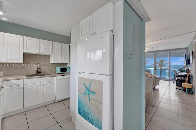 kitchen featuring light tile patterned floors, tasteful backsplash, light countertops, a sink, and white appliances