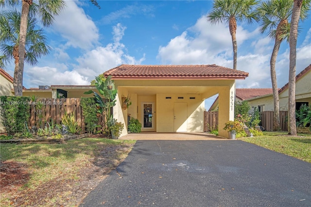 mediterranean / spanish-style house featuring aphalt driveway, fence, a carport, and a tiled roof