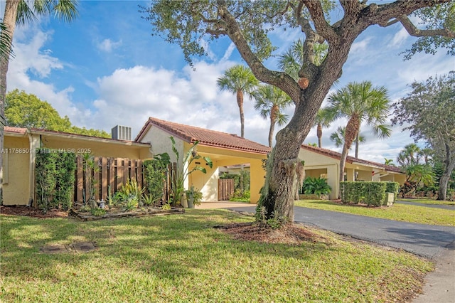 mediterranean / spanish-style house with a tile roof, stucco siding, fence, driveway, and a front lawn