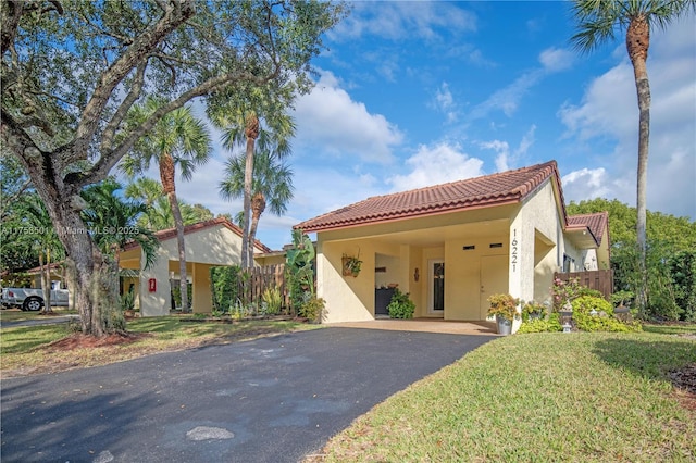 mediterranean / spanish house featuring driveway, a tiled roof, a front lawn, and stucco siding