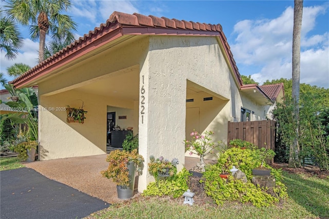 view of side of property featuring stucco siding, a tile roof, and fence