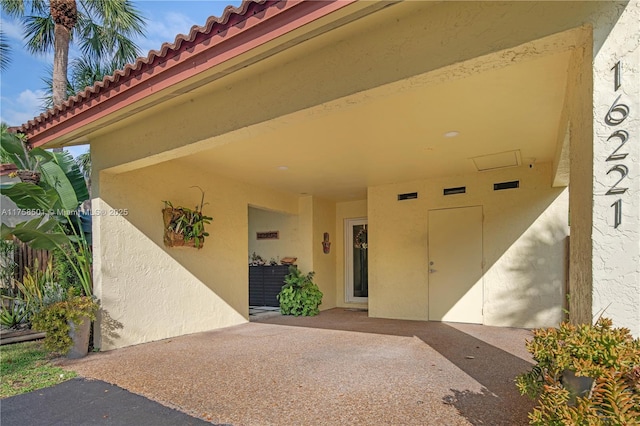 entrance to property with stucco siding, aphalt driveway, a patio area, an attached carport, and a tiled roof