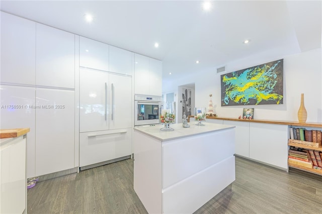 kitchen with light wood-type flooring, a kitchen island, built in fridge, white cabinetry, and white oven