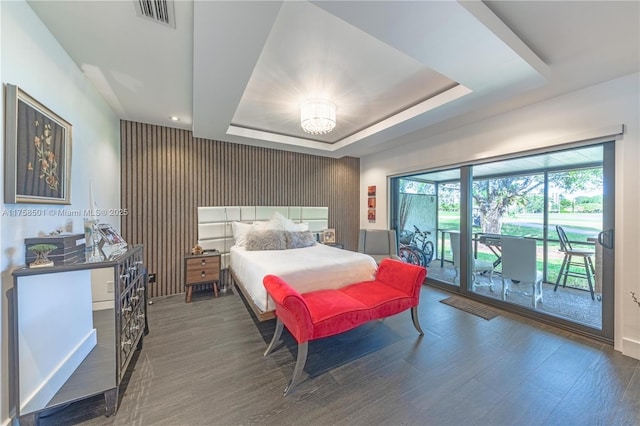 bedroom featuring a tray ceiling, visible vents, wood finished floors, and access to outside