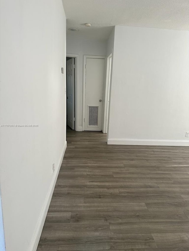 empty room with visible vents, dark wood finished floors, a textured ceiling, and baseboards