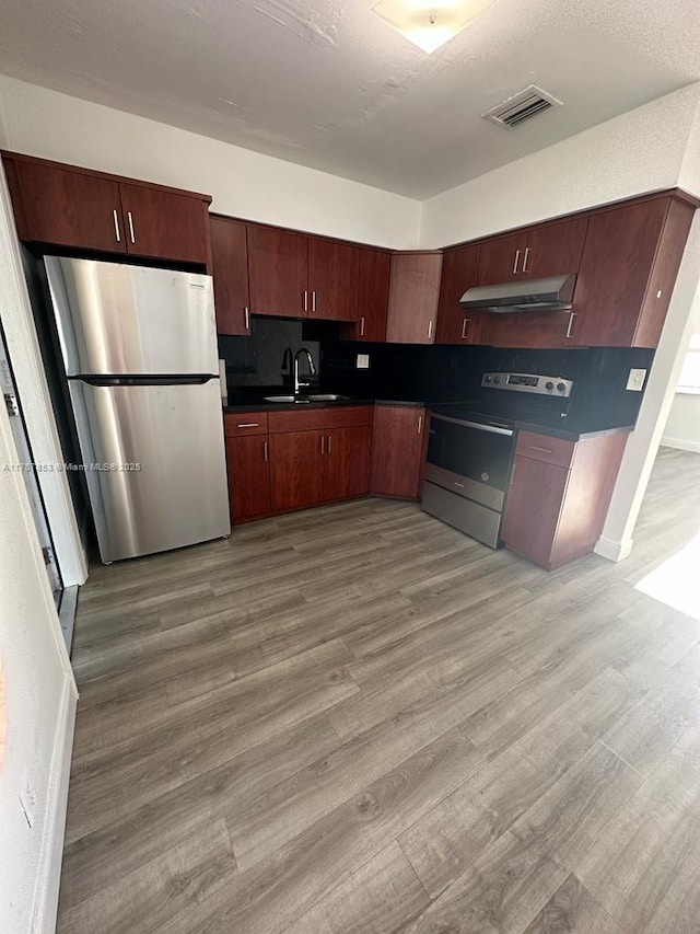 kitchen with stainless steel appliances, dark countertops, visible vents, light wood-style flooring, and a sink