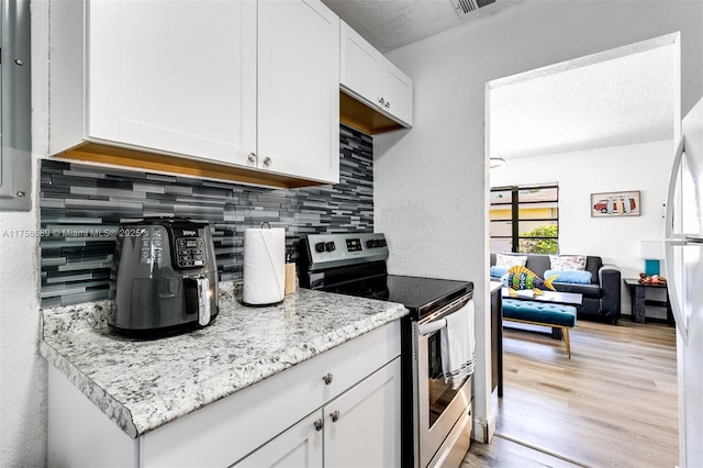 kitchen with backsplash, light wood-style floors, white cabinets, a textured ceiling, and stainless steel electric range