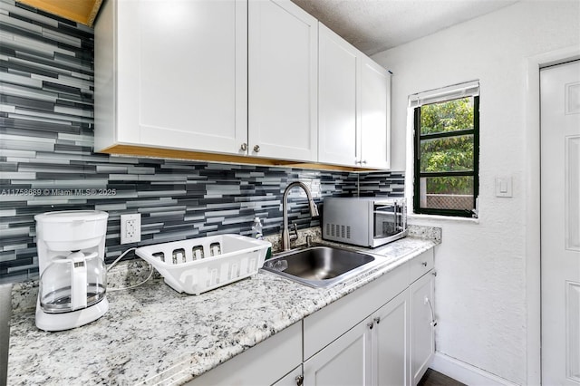 kitchen with white cabinets, stainless steel microwave, a sink, a textured ceiling, and backsplash