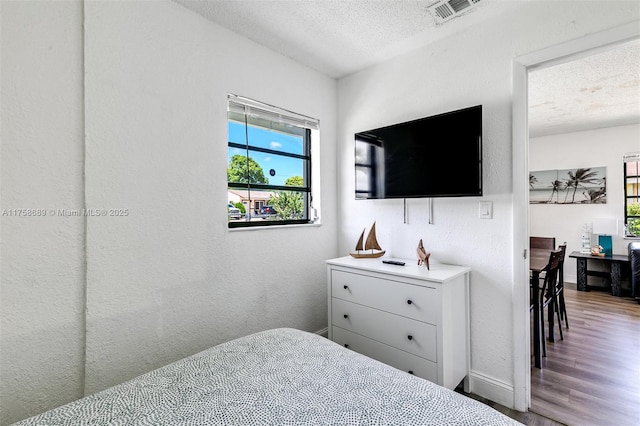 bedroom with visible vents, a textured wall, a textured ceiling, wood finished floors, and baseboards