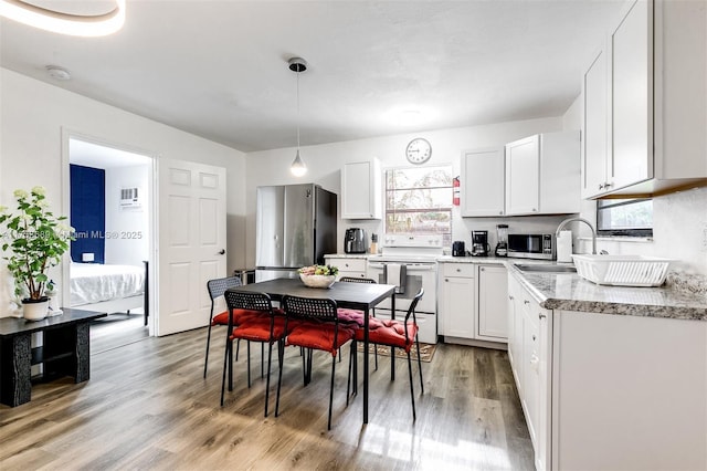 kitchen featuring appliances with stainless steel finishes, white cabinets, a sink, and light wood-style flooring