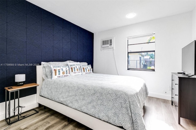 bedroom featuring an accent wall, baseboards, wood finished floors, and a wall mounted air conditioner